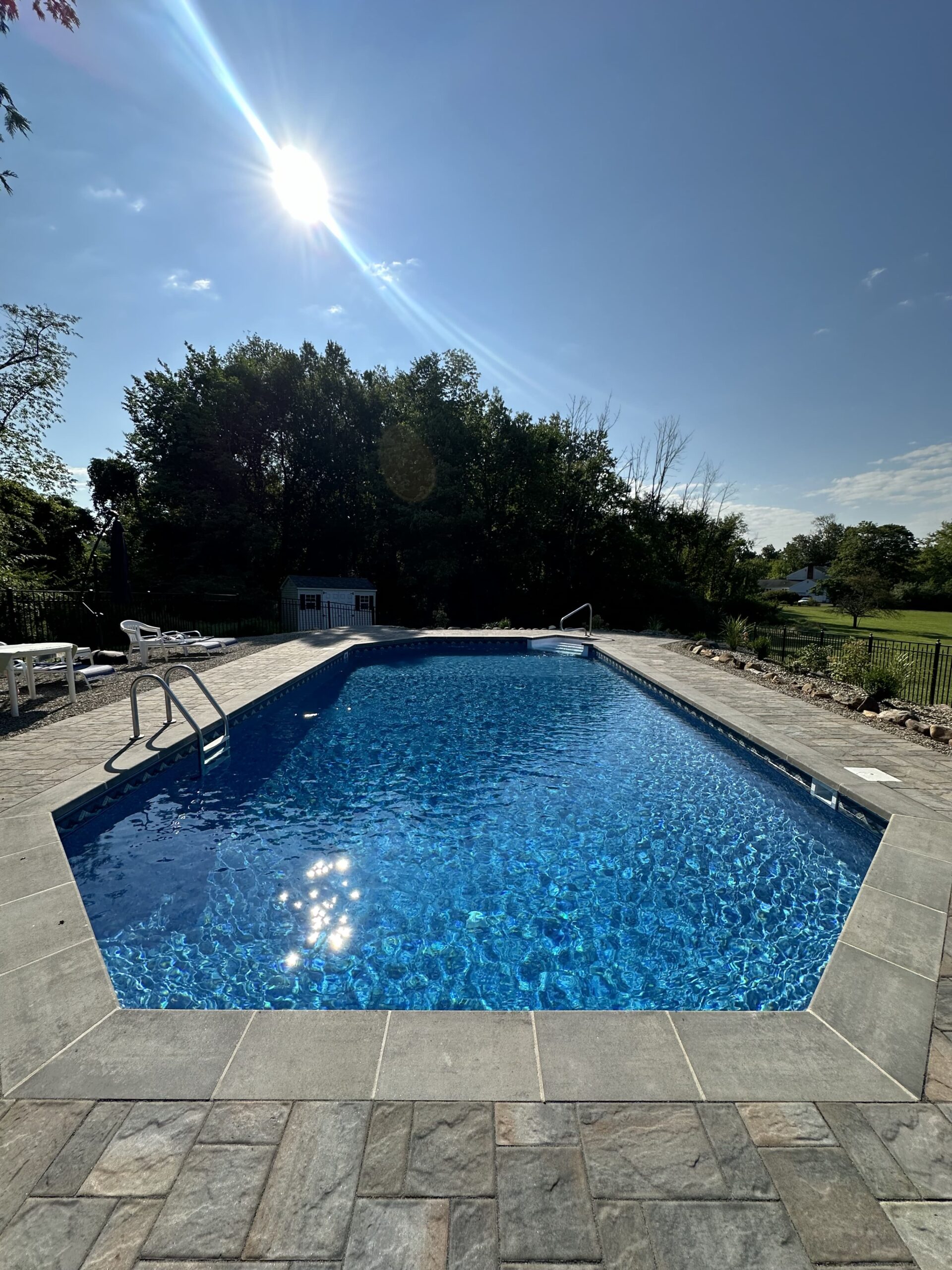 A swimming pool with chairs and trees in the background.